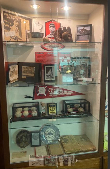 Glass case of Cy Young memorabilia — photographs, a red pennant, baseballs, and gloves