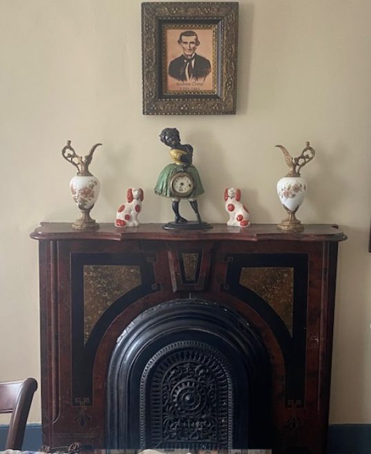 An ornate cast-iron fireplace and mantel with a framed portrait and Victorian mantel pieces